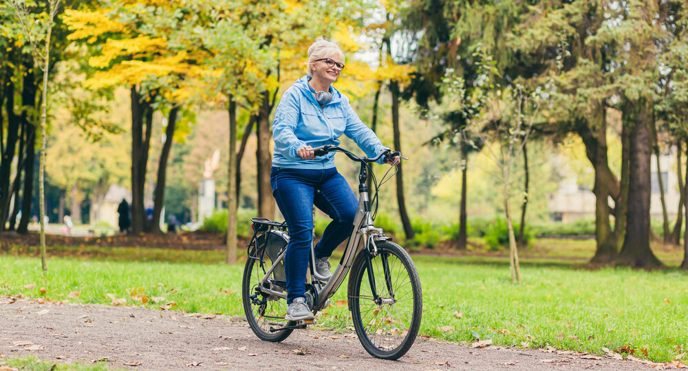 Senior,Woman,Walking,In,The,Park,With,A,Bicycle,,Sunny Older woman biking in nature on a path
